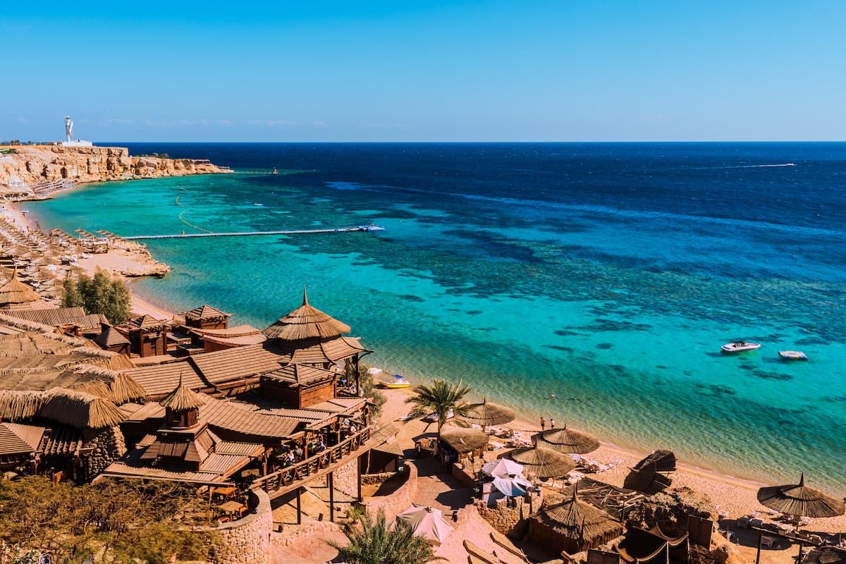 Luftfoto af en bugt ved Sharm el-Sheikh ved Det Røde Hav — restauranter på pæle, turkist vand med koralrev, broer.